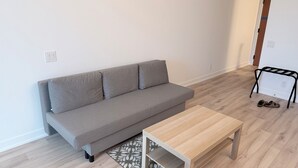 A grey sofa with three cushions, a wooden coffee table, and a small black metal bench with a pair of shoes on it.