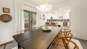 Un'area pranzo moderna con un tavolo in legno scuro, sedie in vimini, un lampadario e vista sulla cucina.