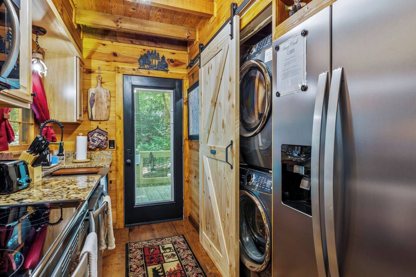 Une cuisine compacte dotée d’un lave-linge et d’un sèche-linge intégrés, d’un intérieur en bois et offrant une vue à travers la porte.