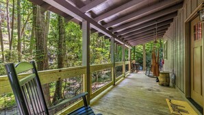Une véranda couverte avec un banc, une balustrade en bois et une vue sur la forêt.