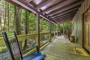 A covered porch with a bench, wooden railing, and a view of the forest. - Creekfront Escape •Firepit •Hiking • Pet Friendly (Blue Ridge)