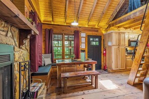 Een landelijk houten interieur met een stenen muur, houten plafond, een eettafel, een bank en een keukenhoek.