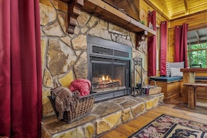 A stone fireplace with a fire, a wicker basket, and a bench with cushions. - Creekfront Escape •Firepit •Hiking • Pet Friendly (Blue Ridge)