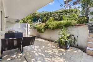 Ein Terrassenbereich im Freien mit einem Esstisch, Stühlen, einem Blumentopf und einer Treppe, die zu einer höheren Ebene führt.