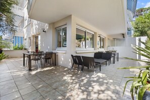Eine überdachte Terrasse mit Sitzgelegenheiten im Freien, großen Fenstern und einem gefliesten Boden.