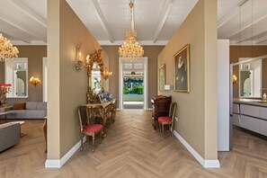 Ein Flur mit Fischgratparkett, einer Chandelierleuchtre, einem Esstisch mit Stühlen und einer Küchenzeile inklusive Kühlschrank.