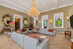 Ein geräumiges Wohnzimmer mit einem großen Kronleuchter, mehreren Sofas und dekorativen Spiegeln.