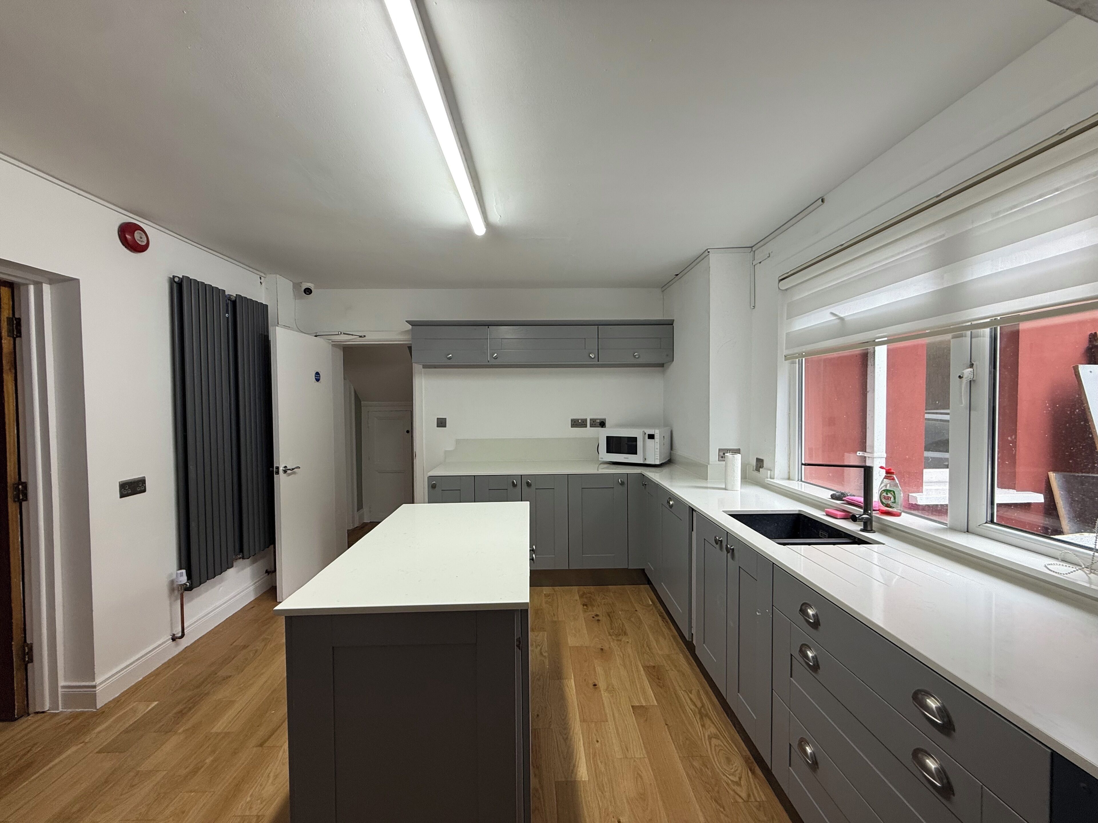 A modern kitchen with a central island, grey cabinets, a microwave, and a window with a view.