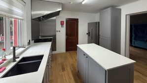 Uma cozinha moderna com armários brancos, exaustor de aço inoxidável, forno embutido e geladeira.