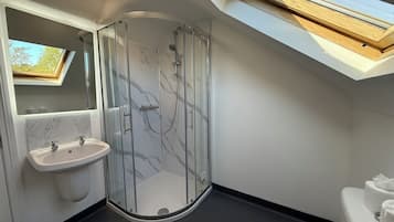 Un baño moderno con ducha envuelta en vidrio, tocador de mármol y tragaluz.