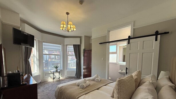Quarto de hotel com cama, escrivaninha, televisão, lustre e vista da cidade.