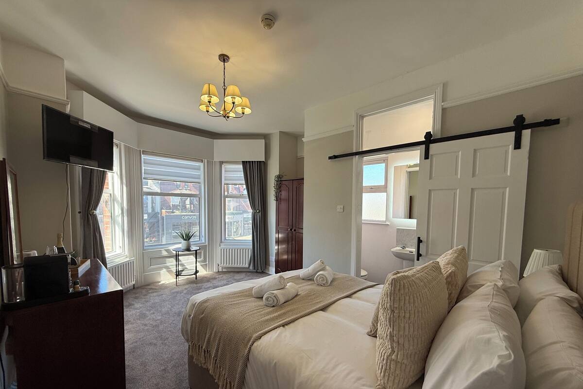 A hotel room with a bed, a desk, a TV, a chandelier, and a view of the city.