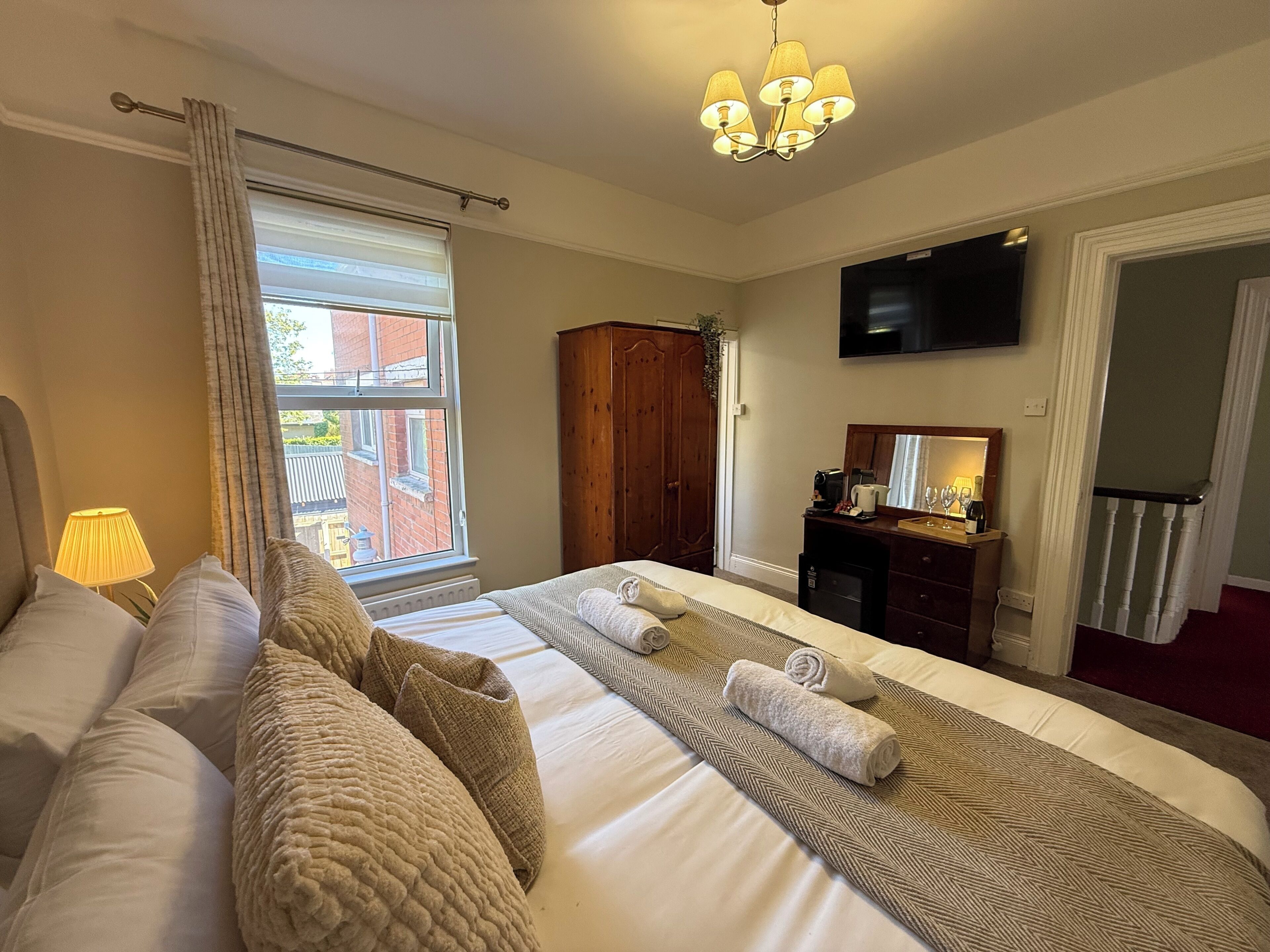 Habitación de hotel con cama, televisión, escritorio con espejo y ventana con cortinas.