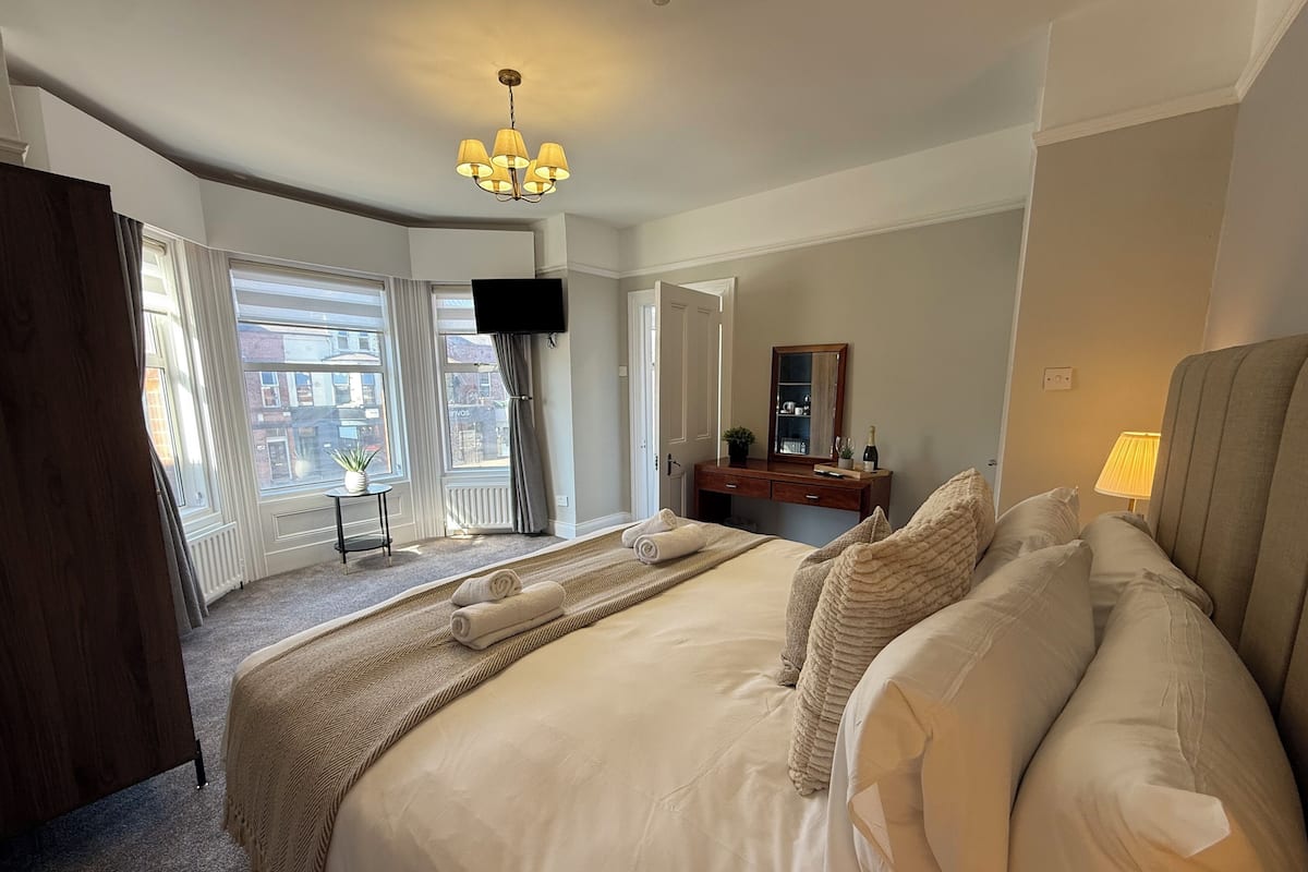 A hotel room with a large bed, a TV, a dresser, a mirror, and a window with curtains.