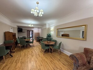 A room with a wooden floor, green chairs, a round table, a chandelier, a large mirror, and a television on the wall.