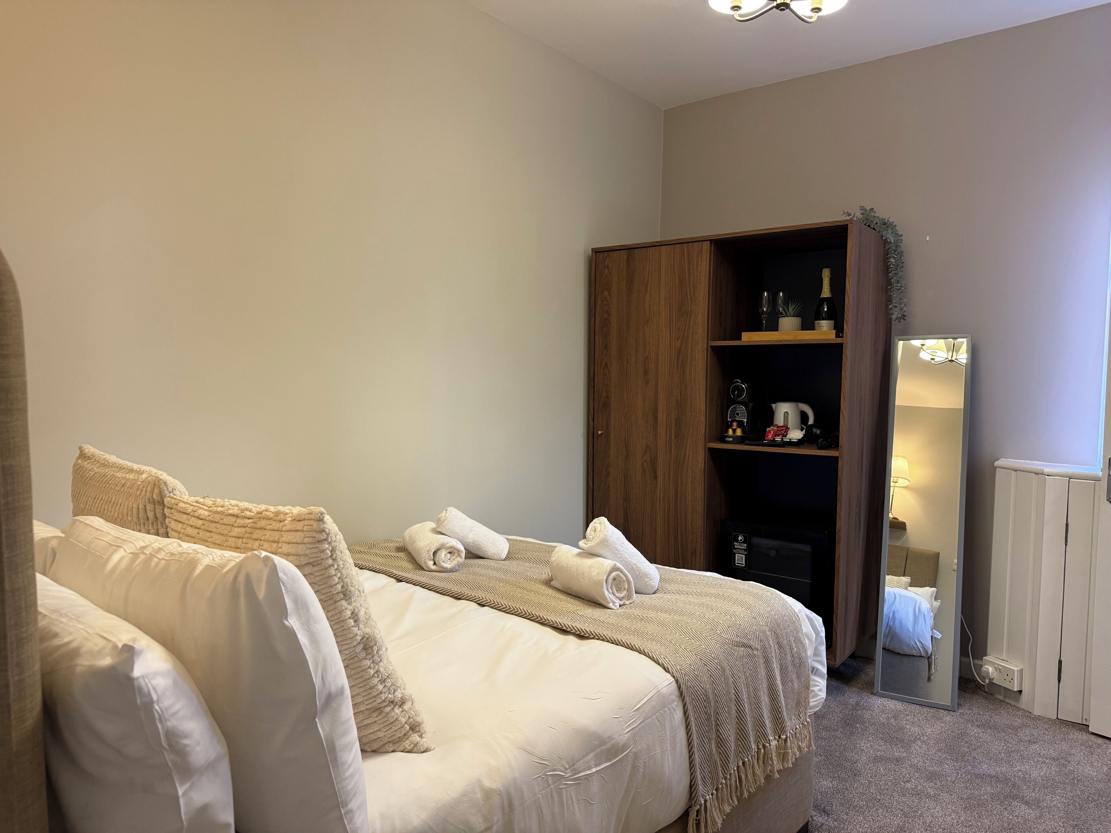 A bedroom with a bed, a wardrobe, a mirror, and a shelf with items.