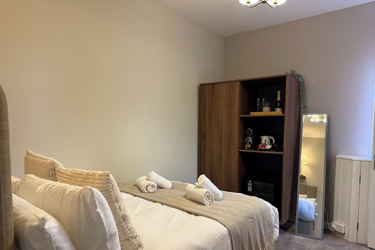 A bedroom with a bed, a wardrobe, a mirror, and a shelf with items.