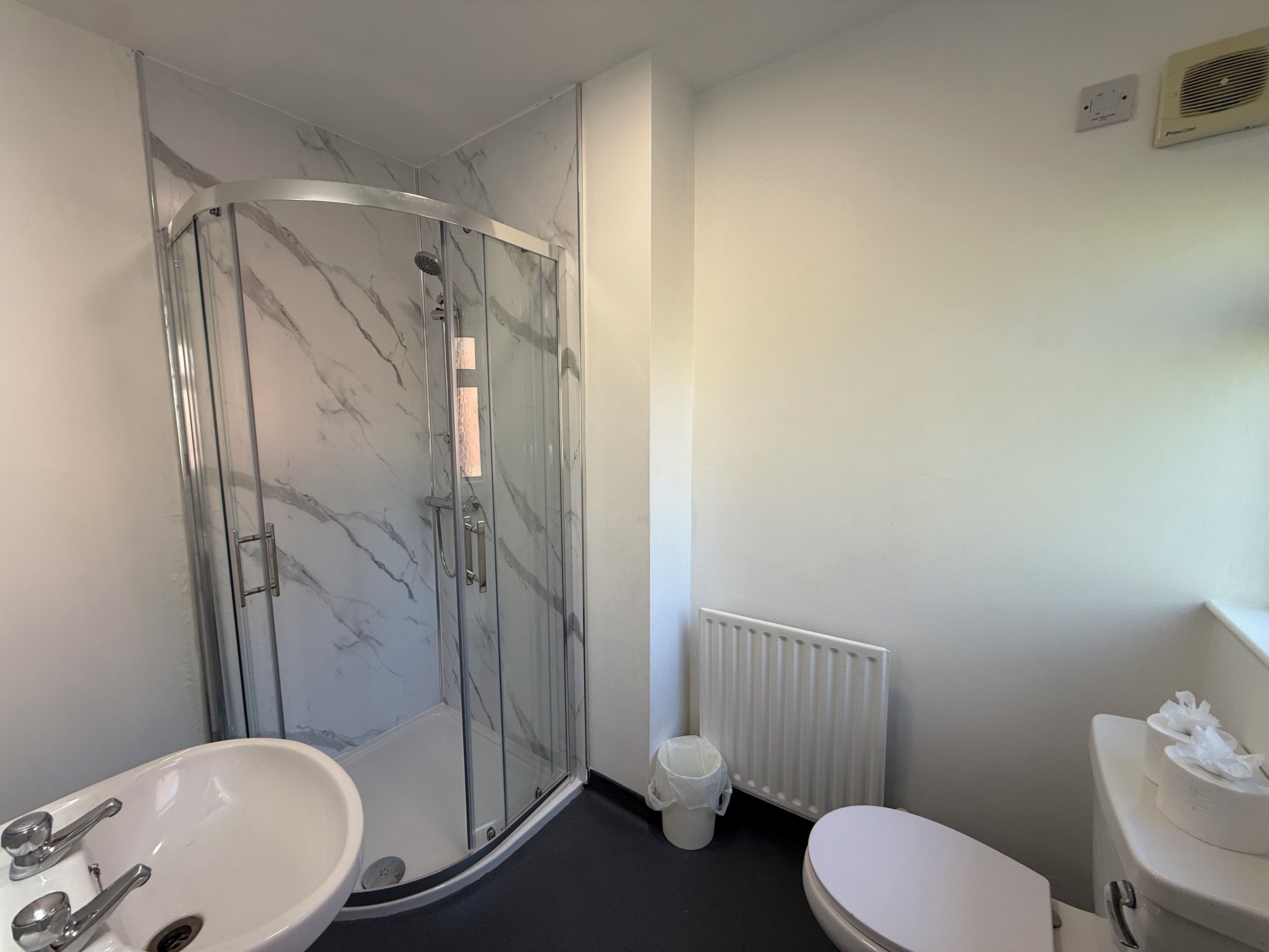 Un baño con ducha de vidrio, lavamanos blanco y retrete.