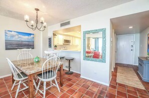 A dining area with a table, chairs, a chandelier, a kitchen with a microwave, and a mirror. - Soulside 5G by Mira-Mar (Wrightsville Beach)