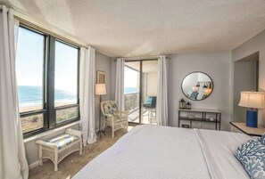 Ein Hotelzimmer mit einem großen Bett, einem Sessel, einem Schreibtisch, einem Spiegel und Blick auf den Strand.