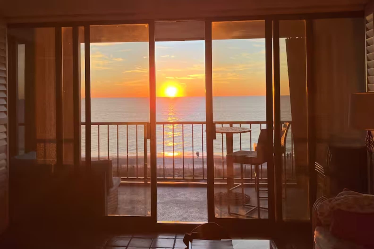 Ein Zimmer mit Blick auf den Sonnenuntergang über dem Meer, ein Balkon mit Stühlen und einem Tisch.