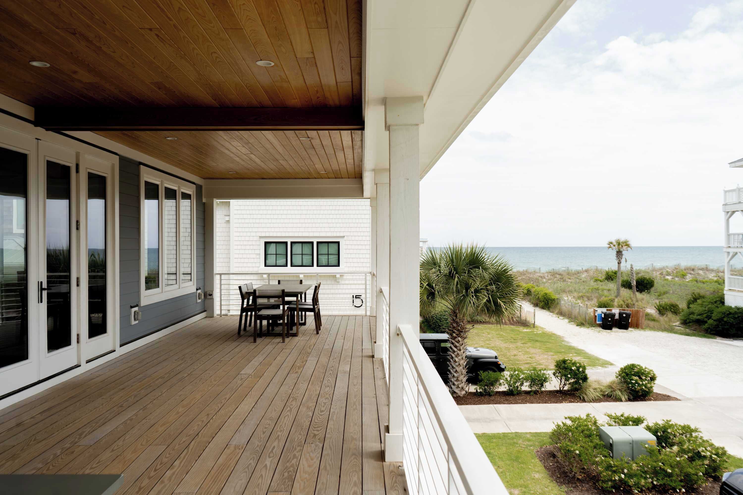 A covered deck with a table and chairs, a view of the ocean, and a white building with a garage.