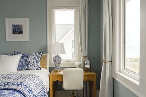 Ein Zimmer mit einem Bett, einem Schreibtisch mit Lampe, einem Stuhl, einem gerahmten Bild und einem Fenster mit Vorhängen.