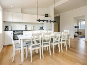 A modern kitchen with white cabinetry, a dining table with chairs, and a black hanging light fixture. - 5 Star Holiday Home in Saltum (Saltum)
