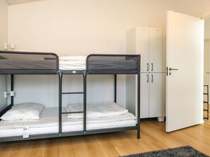 Ein Stockbett mit einer Stehle, ein weißer Kleiderschrank und eine Tür in einem Zimmer mit Holzboden.