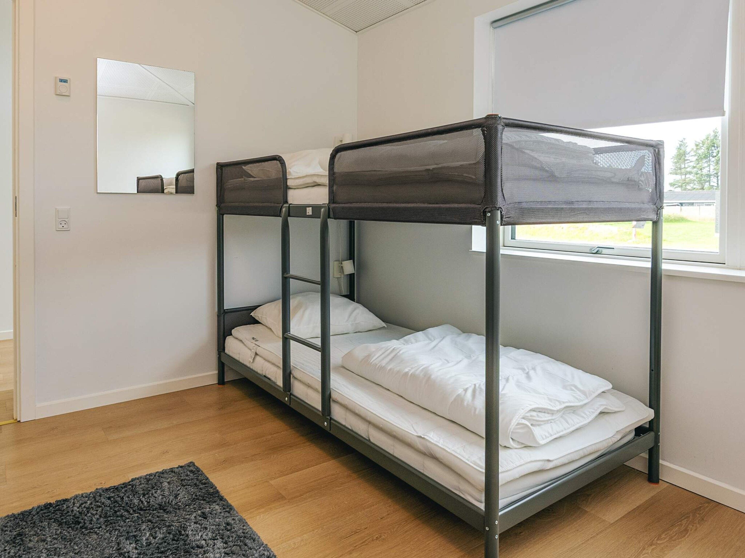 A bunk bed room with a window, a mirror, and a rug.