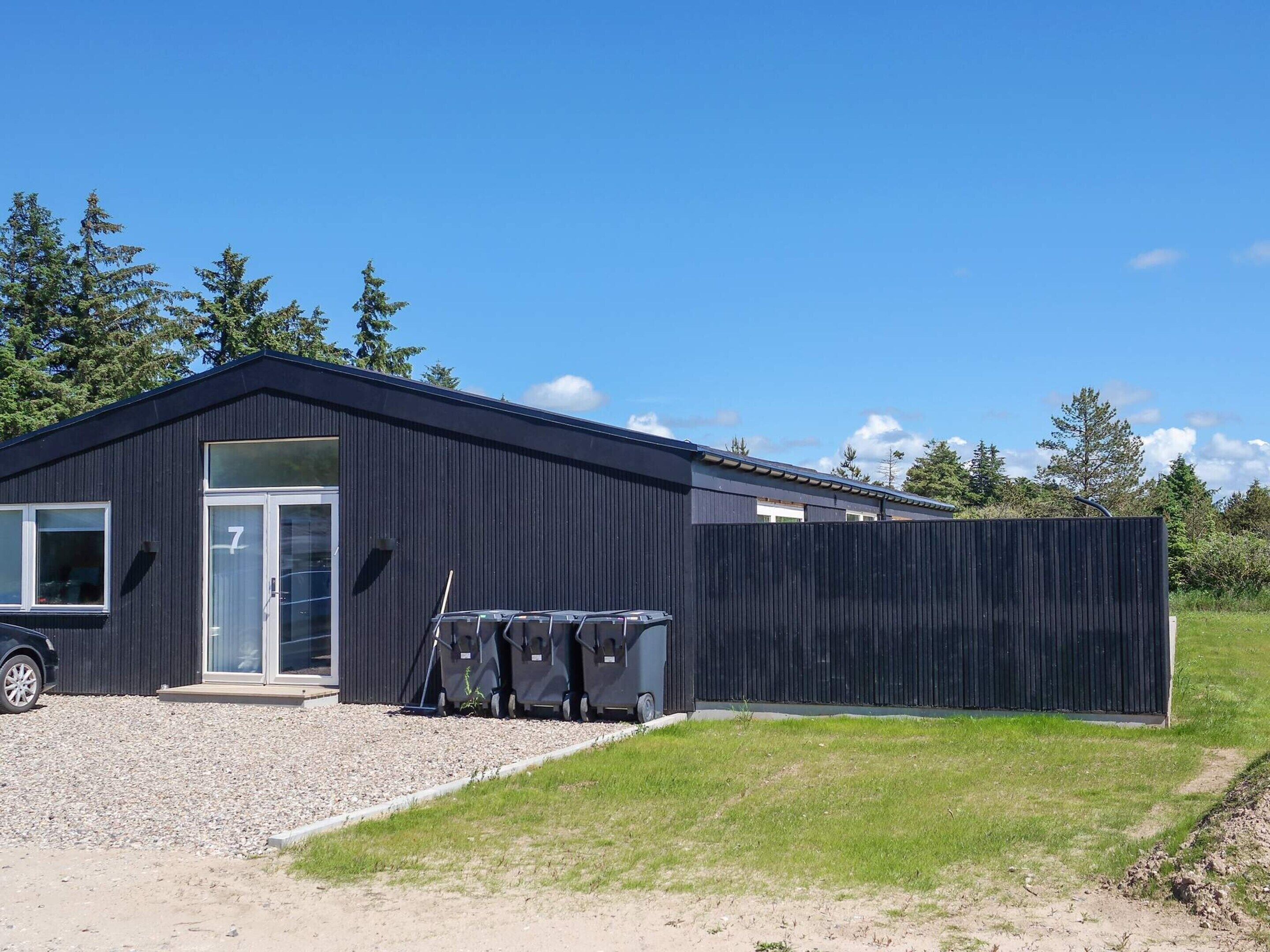 A modern building with a dark exterior, a large glass door, and a gravel driveway.