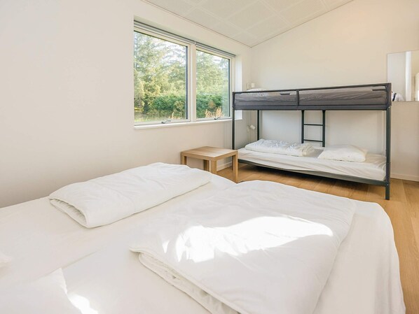 A bedroom with two beds, a window, a bedside table, and a bunk bed. - 5 Star Holiday Home in Saltum (Saltum)