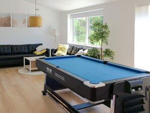 Ein Billardtisch in einem Wohnzimmer mit einer Couch, einem kleinen Tisch und einer Lampe.