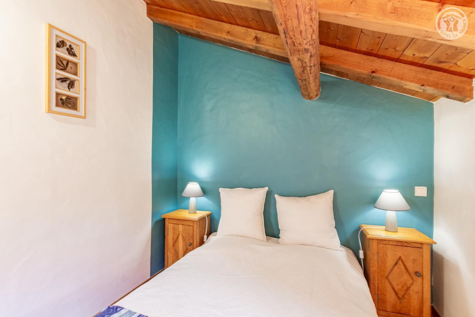 A bedroom with a teal-colored headboard, a wooden ceiling, and two bedside lamps.