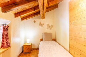Ein Schlafzimmer mit Holzbalkendecke, einem Bett mit weißer Decke, einem Nachttisch mit Lampe und Wanddekorationen mit Schmetterlingen.