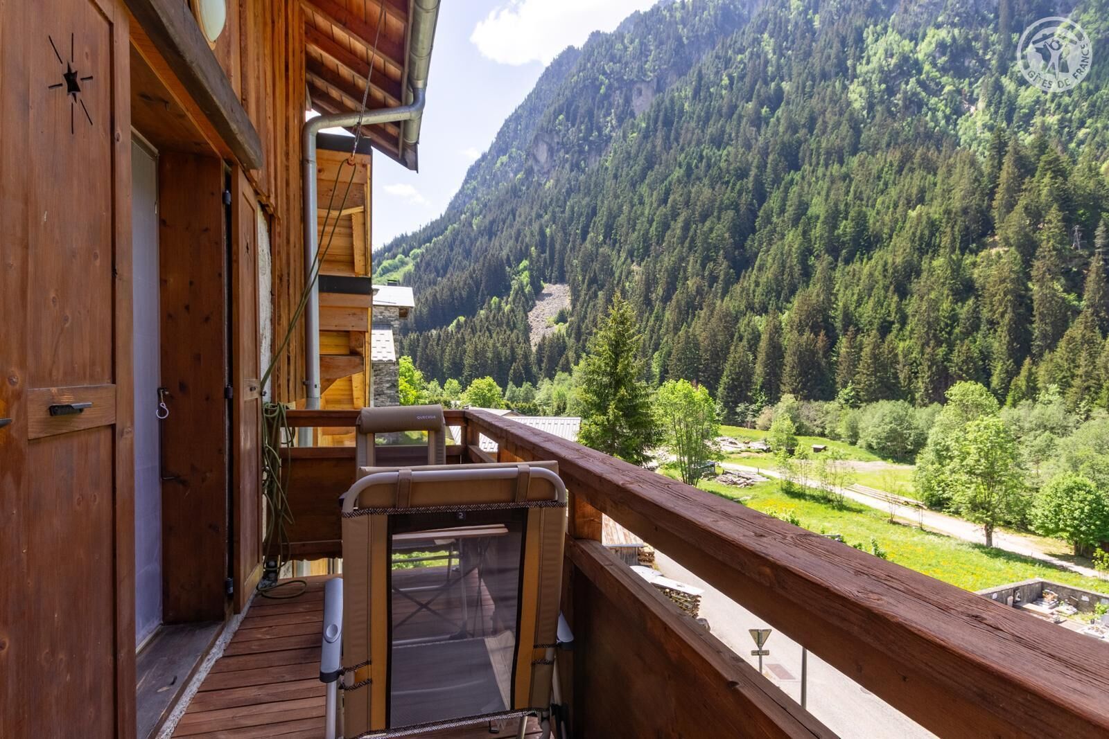 A wooden balcony with a view of a forested valley and mountains.