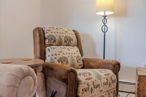Un sillón de cuero marrón con cojines estampados, una mesita auxiliar de madera redonda y una lámpara de pie.