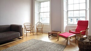 Ein Wohnzimmer mit einer Couch, zwei Korbstühlen, einem roten Sessel, einem kleinen Tisch und einem Teppich.