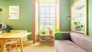 Ein Zimmer mit Holztisch, gepolsterten Sitzbänken, einer Couch und einem Bücherregal mit Pflanzen.
