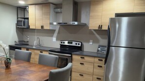 A modern kitchen with a dining table, chairs, a refrigerator, a stove, and cabinets.