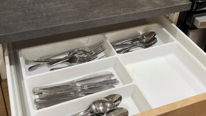 A kitchen with a drawer containing utensils, a stove, and a power outlet on the wall.
