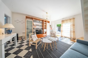 Ein Wohnzimmer mit einer Couch, zwei Sesseln, einem Couchtisch, einem Fernseher und einem Bücherregal.