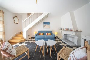 Ein Wohnzimmer mit einem blauen Sofa, zwei weißen Tischen, einem Kamin, einer Treppe und einem Schachbrettmuster-Boden.