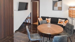 A dining area with a round table, grey upholstered chairs, a sofa with patterned cushions, a TV mounted on the wall, and a wooden door. - 2 bedroom gorgeous apartment in Okrug Gornji (Okrug Gornji)