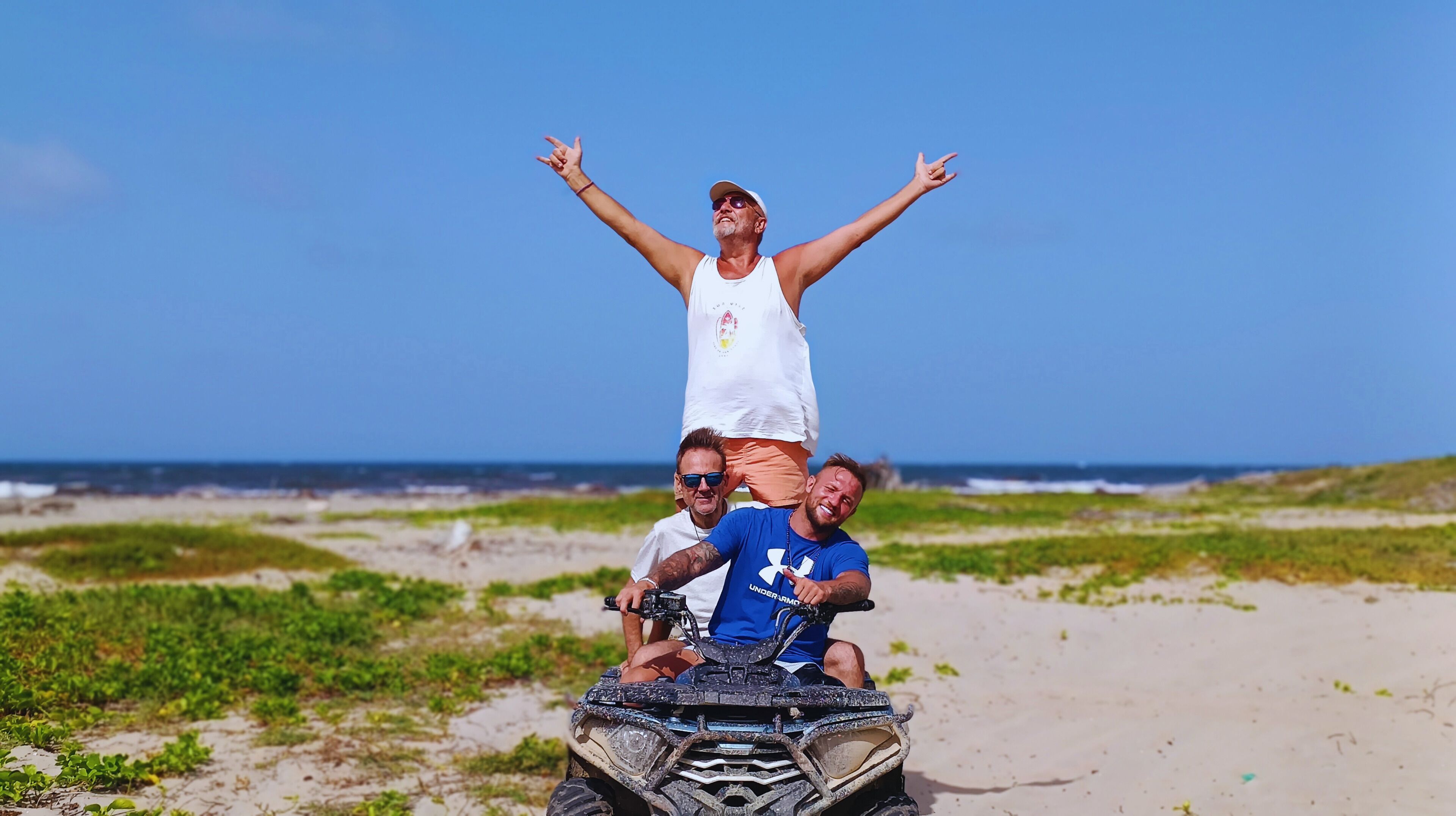 Three people on an ATV on a beach with a clear sky.