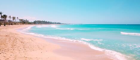 A beach with clear turquoise waters, sandy shore, and palm trees.