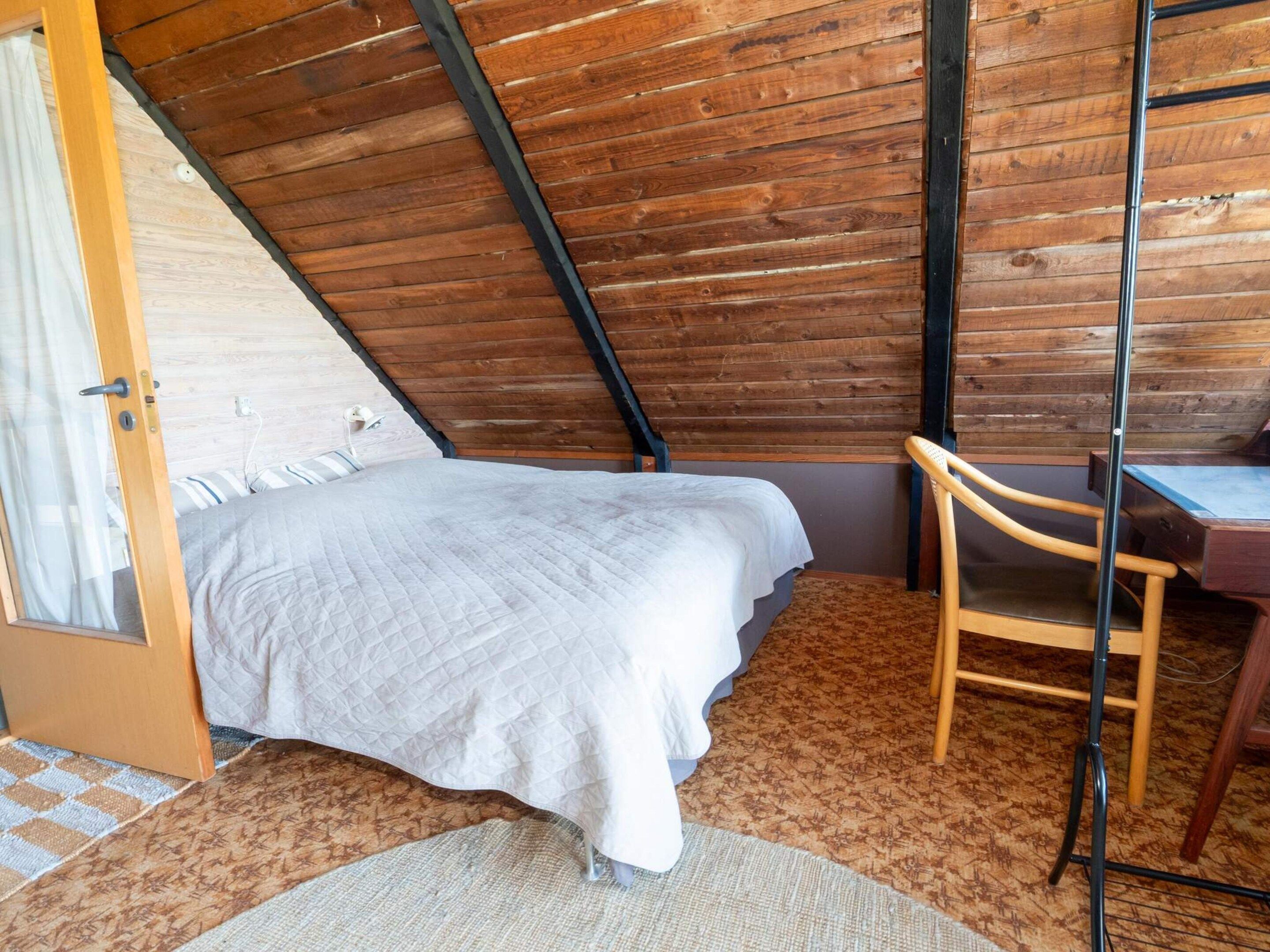 Une chambre avec un plafond en pente, un lit, un bureau et une chaise.