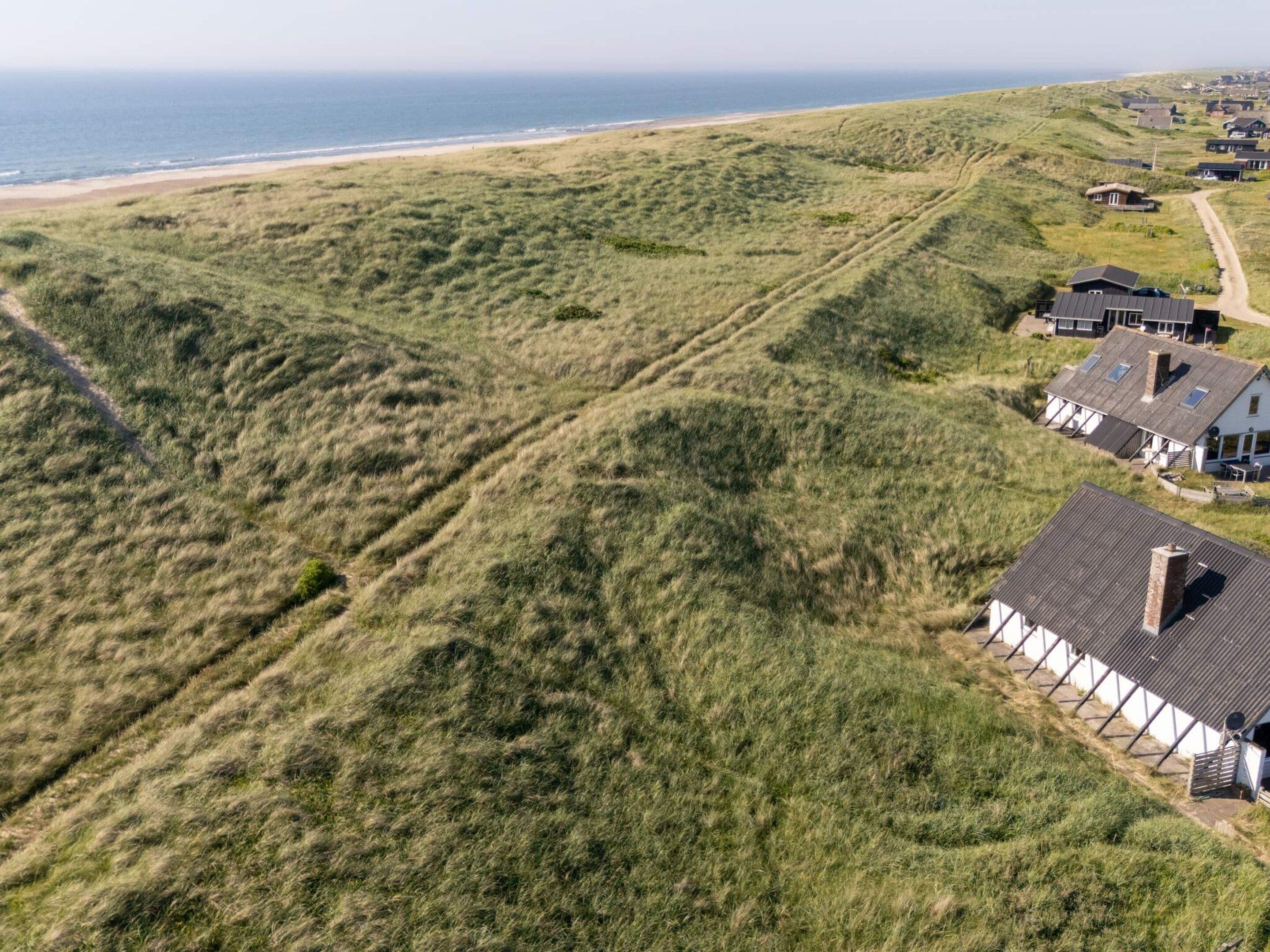 Un paysage côtier avec des maisons construites sur des dunes, une plage et un ciel dégagé.