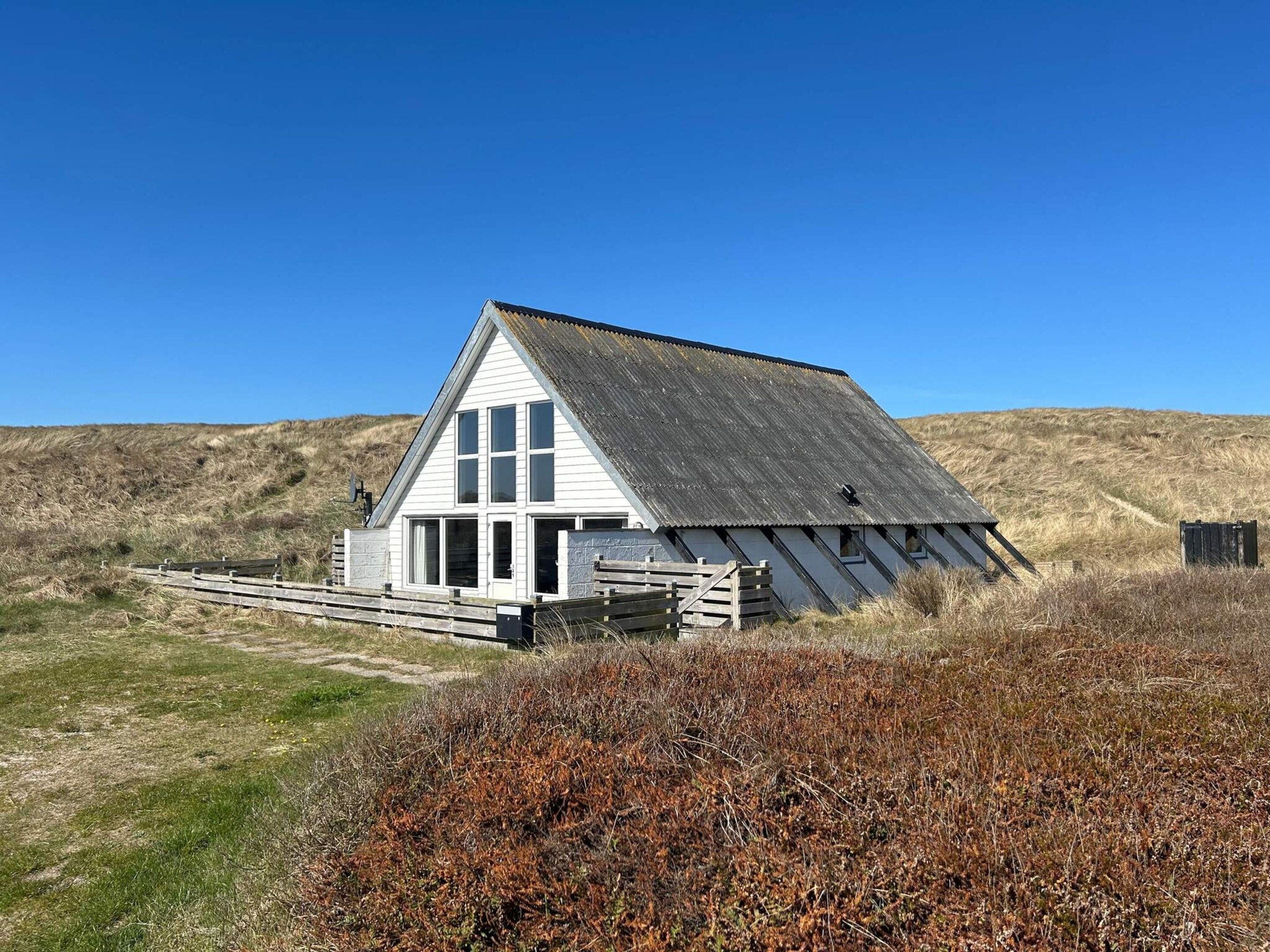 A white building with a sloped roof, a wooden deck, and a clear sky.