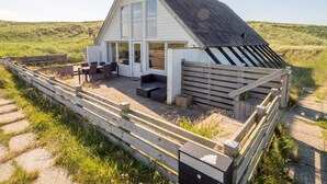 Une maison avec un toit en pente, de grandes fenêtres et un patio aménagé avec du mobilier d’extérieur.
